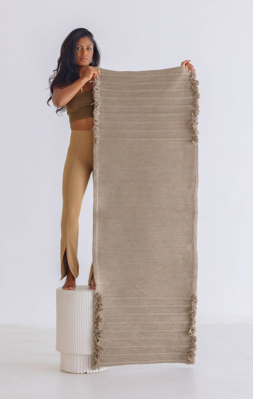 Woman standing on a stool and holding up a  beige yoga mat on a white background