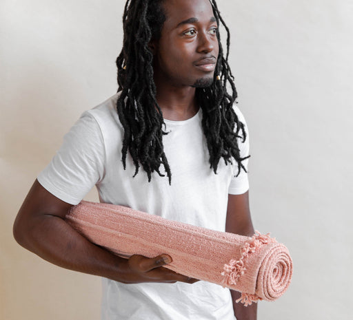 Man holding a pink yoga mat against a plain background