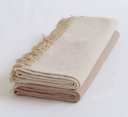 Folded beige yoga mat with tassles on a white background